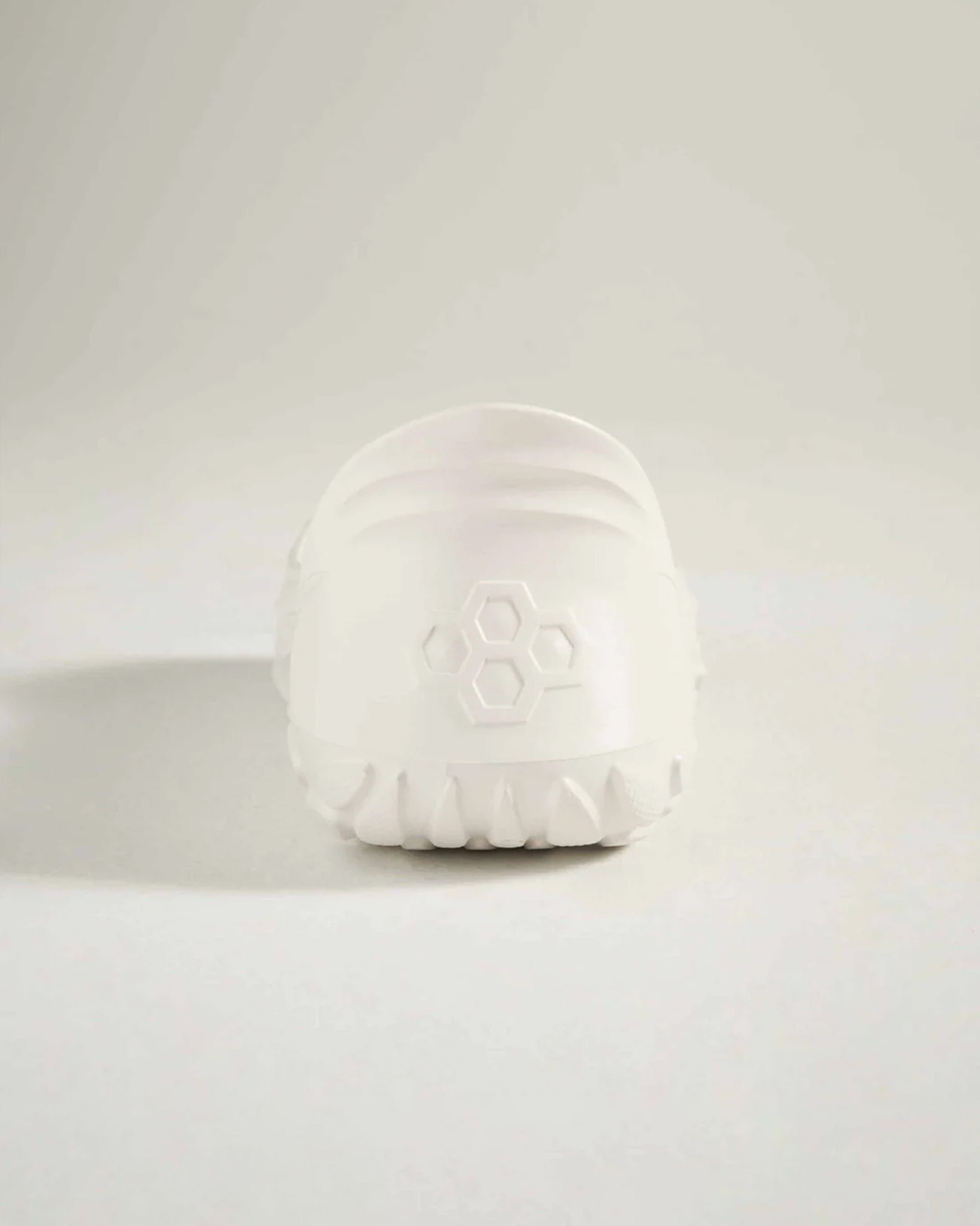 A minimalist white shoe showcasing a smooth rounded silhouette with a textured sole for traction