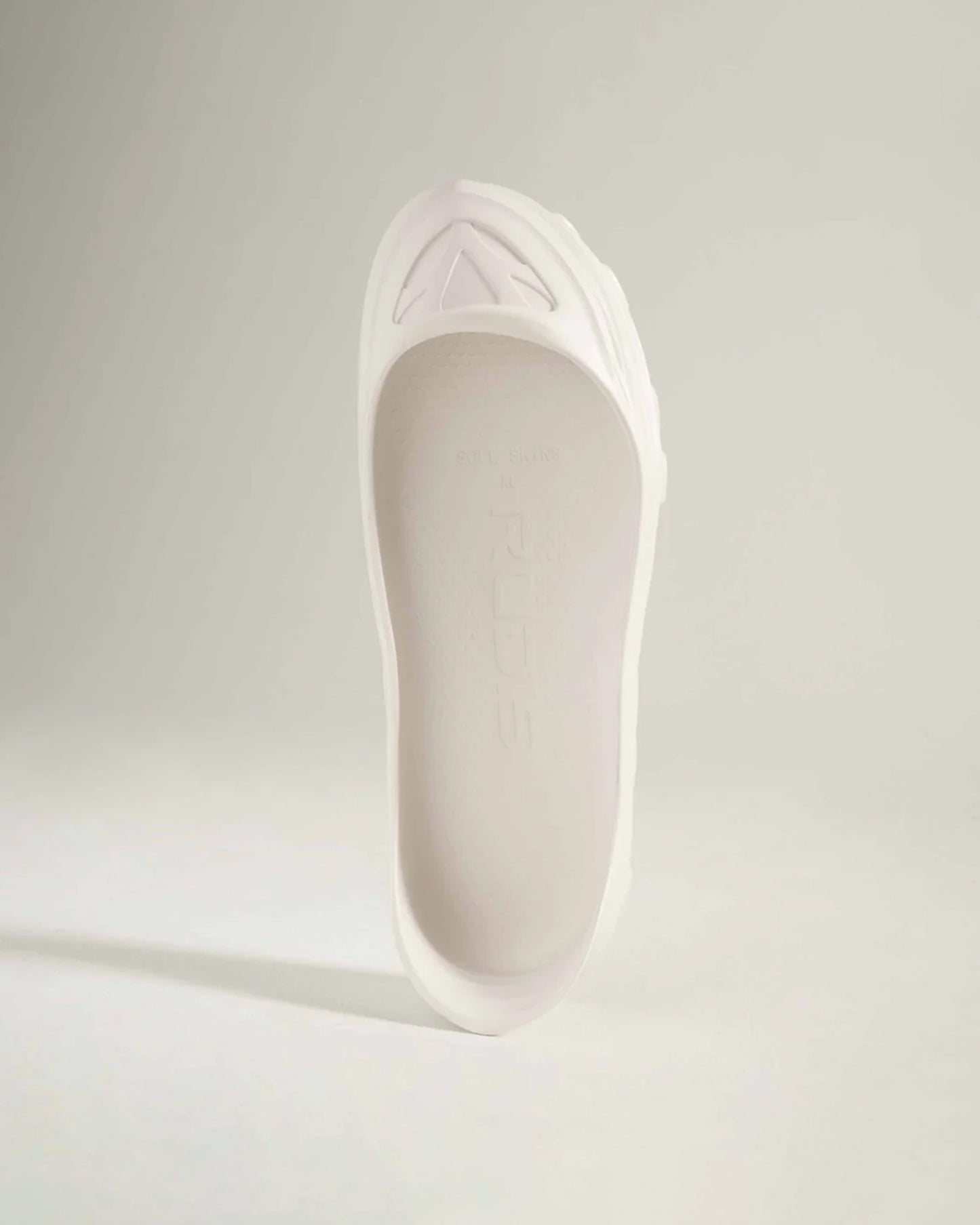 An elegant white shoe with a smooth finish and a structured design showcasing a unique sole and minimalistic aesthetic