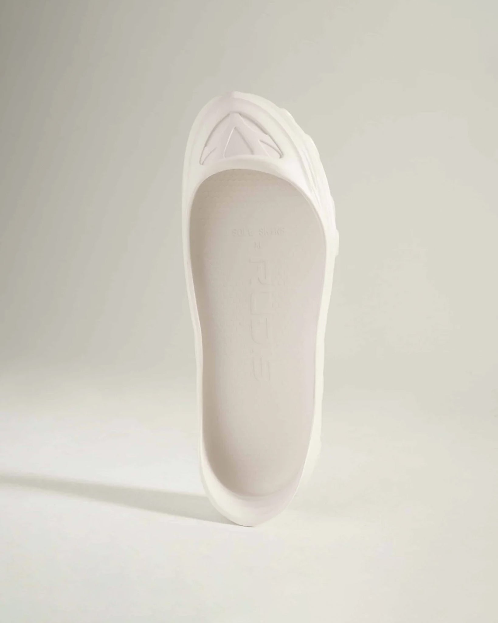 An elegant white shoe with a smooth finish and a structured design showcasing a unique sole and minimalistic aesthetic
