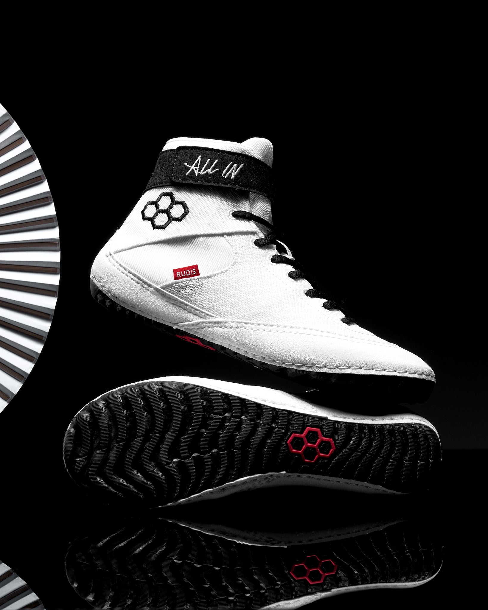 White wrestling shoes with black soles on a reflective surface with a black background