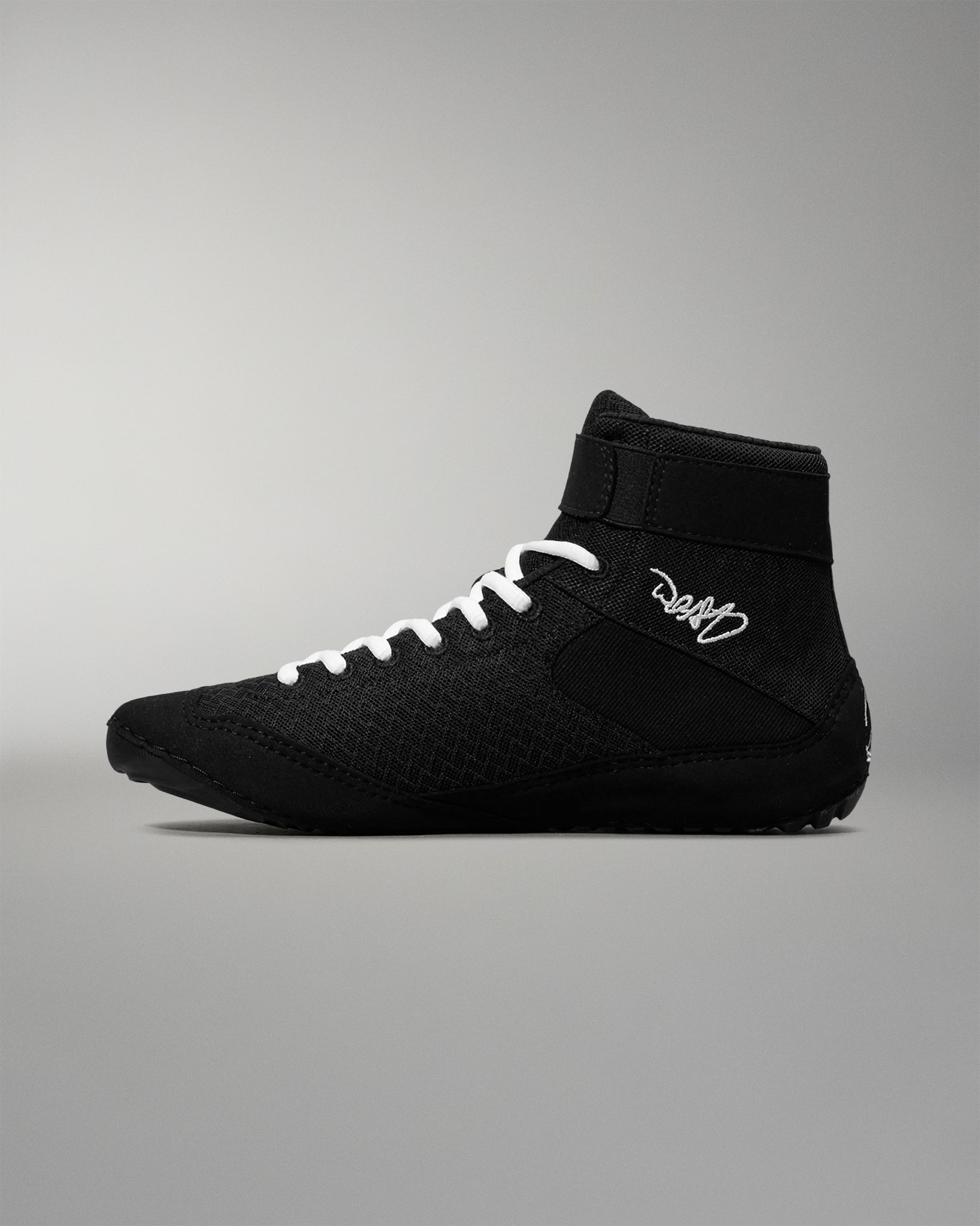 Black wrestling shoe with white laces on a gray background