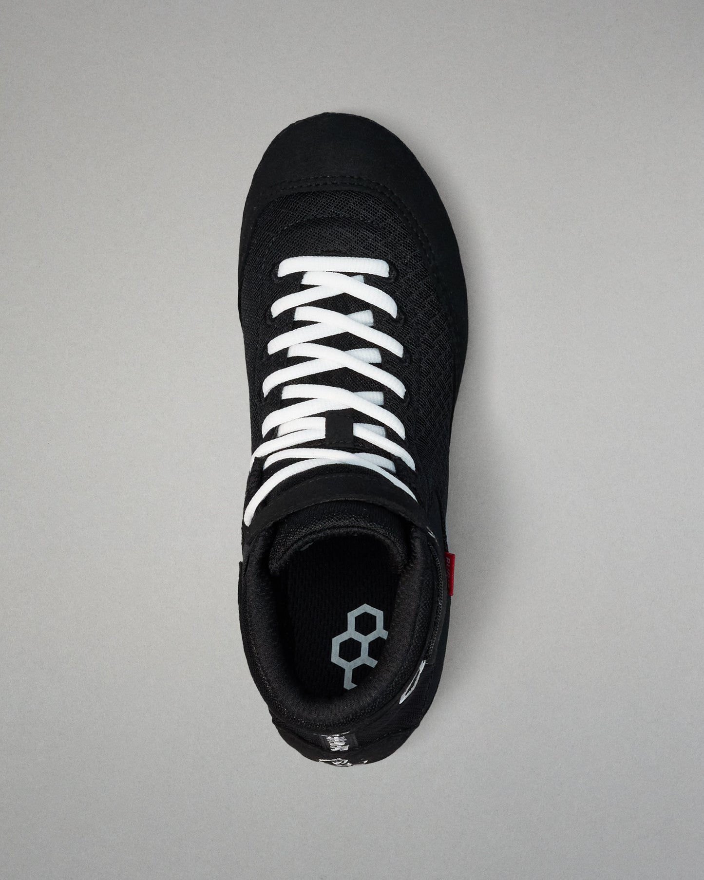 Black wrestling shoe with white laces on a gray background