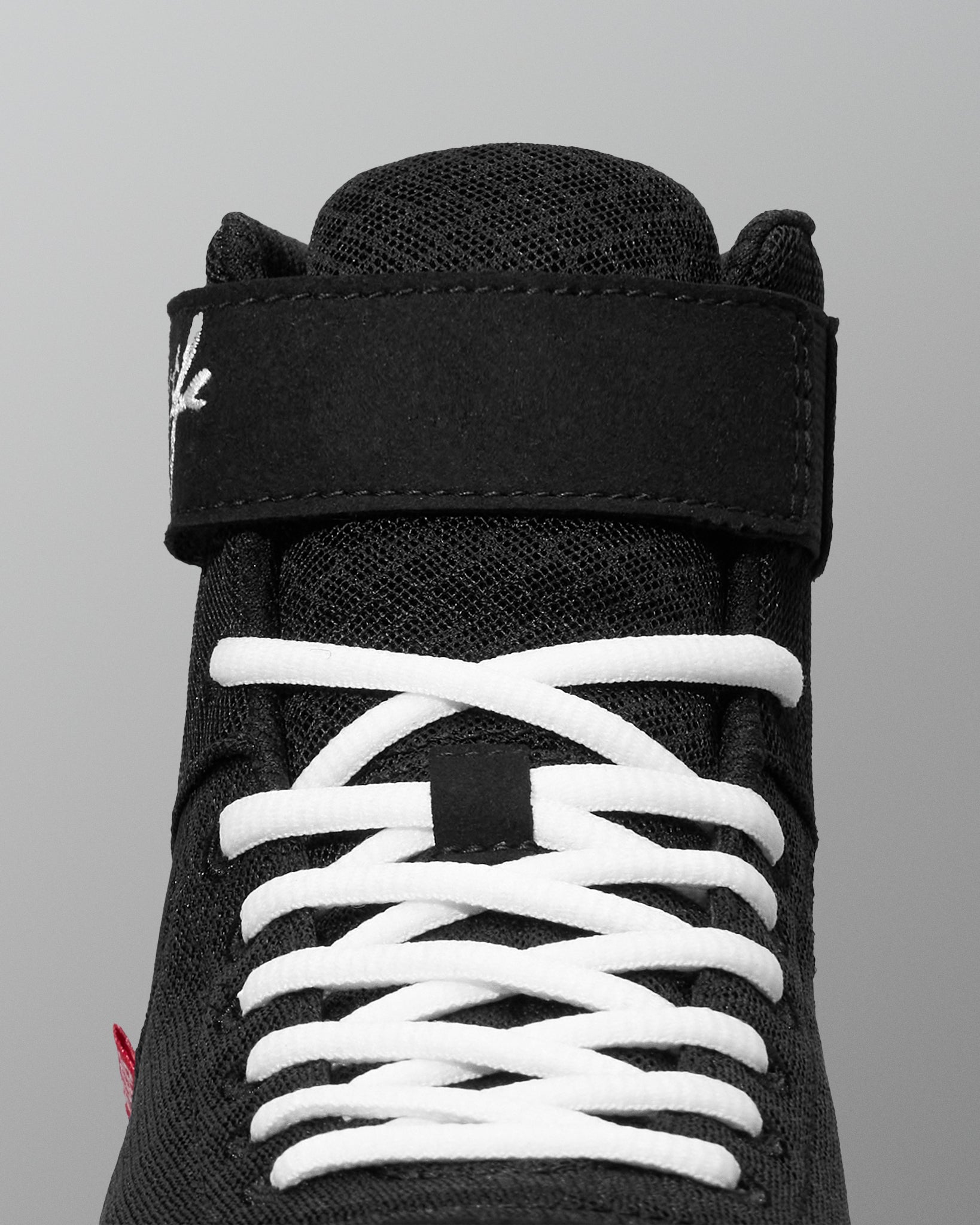 Black wrestling shoe with white laces on a gray background