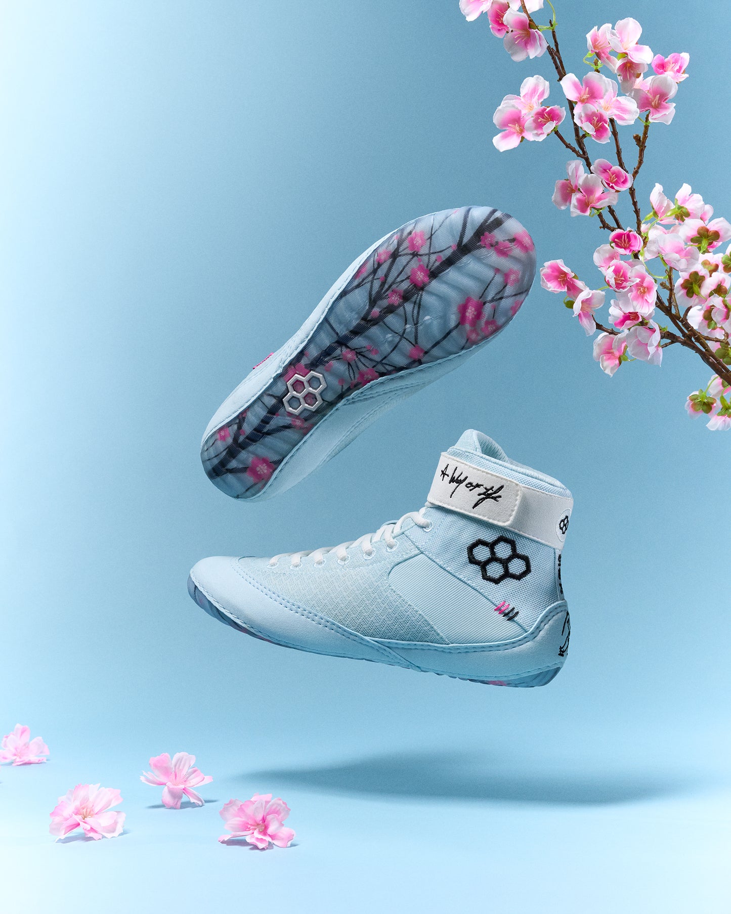 Light blue wrestling shoes with floral design on a light blue background with pink flowers.