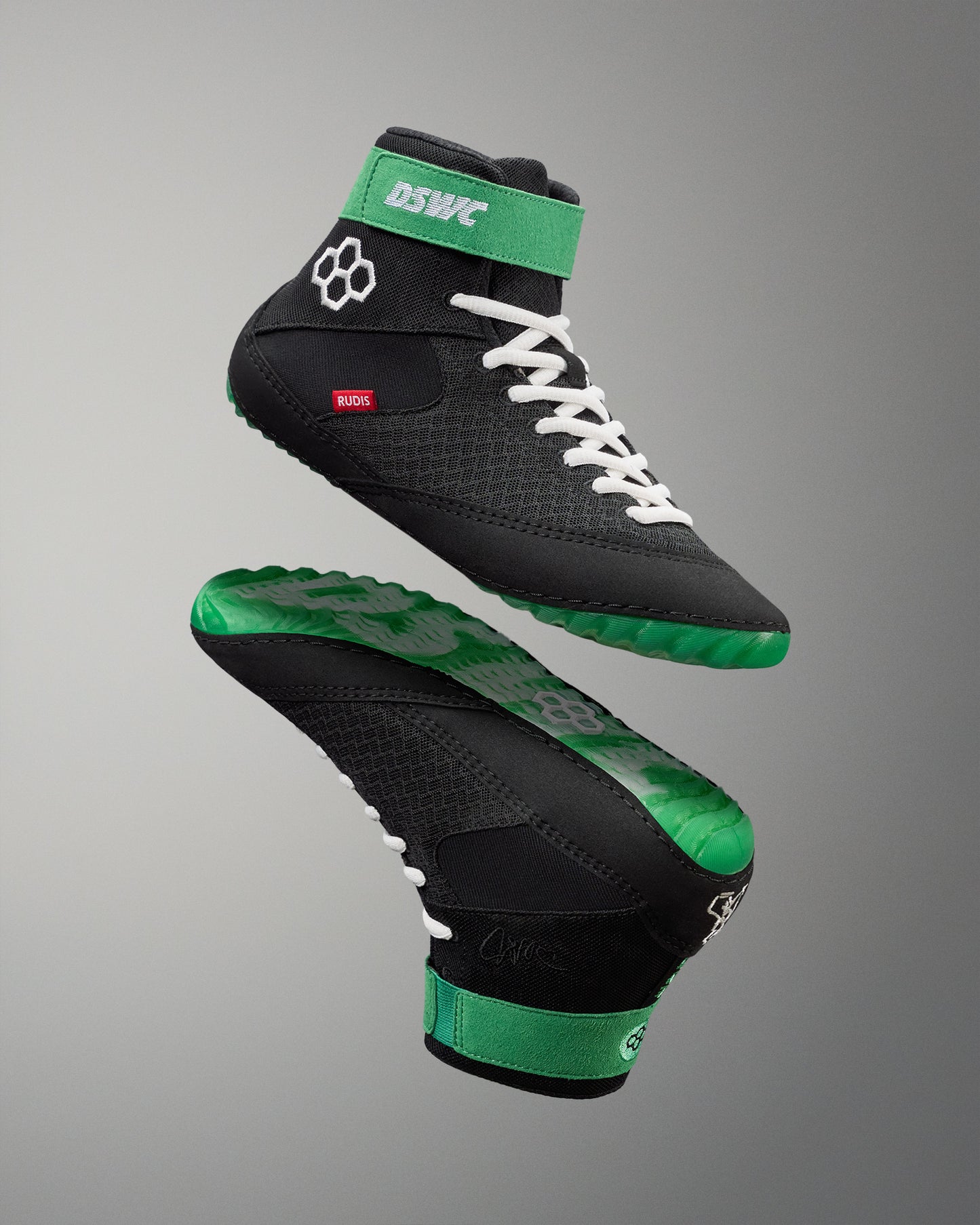 Black and green wrestling shoes with white laces on a gray background