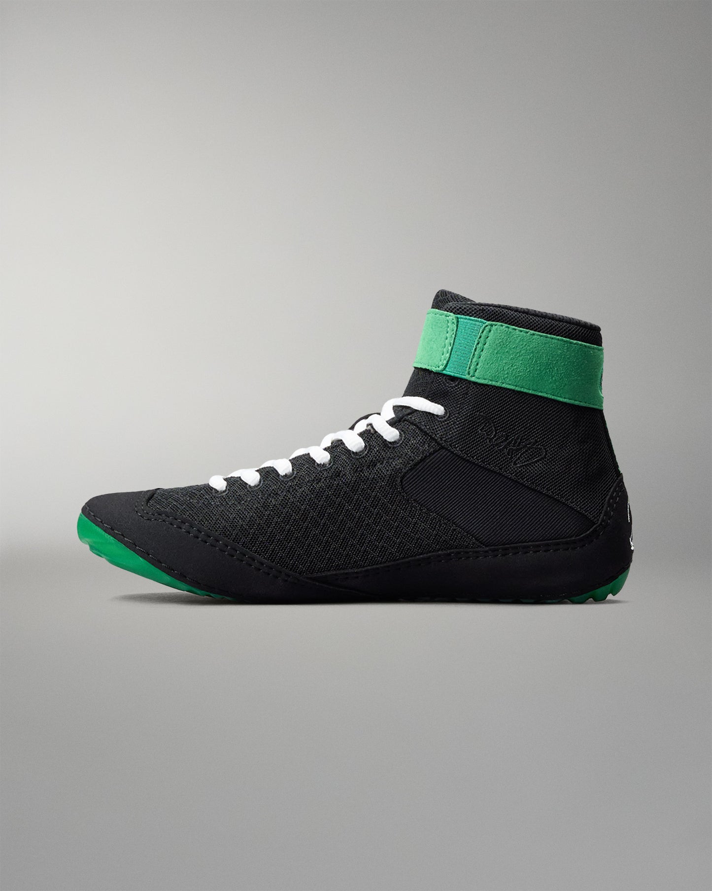 Black wrestling shoe with green accents on a gray background