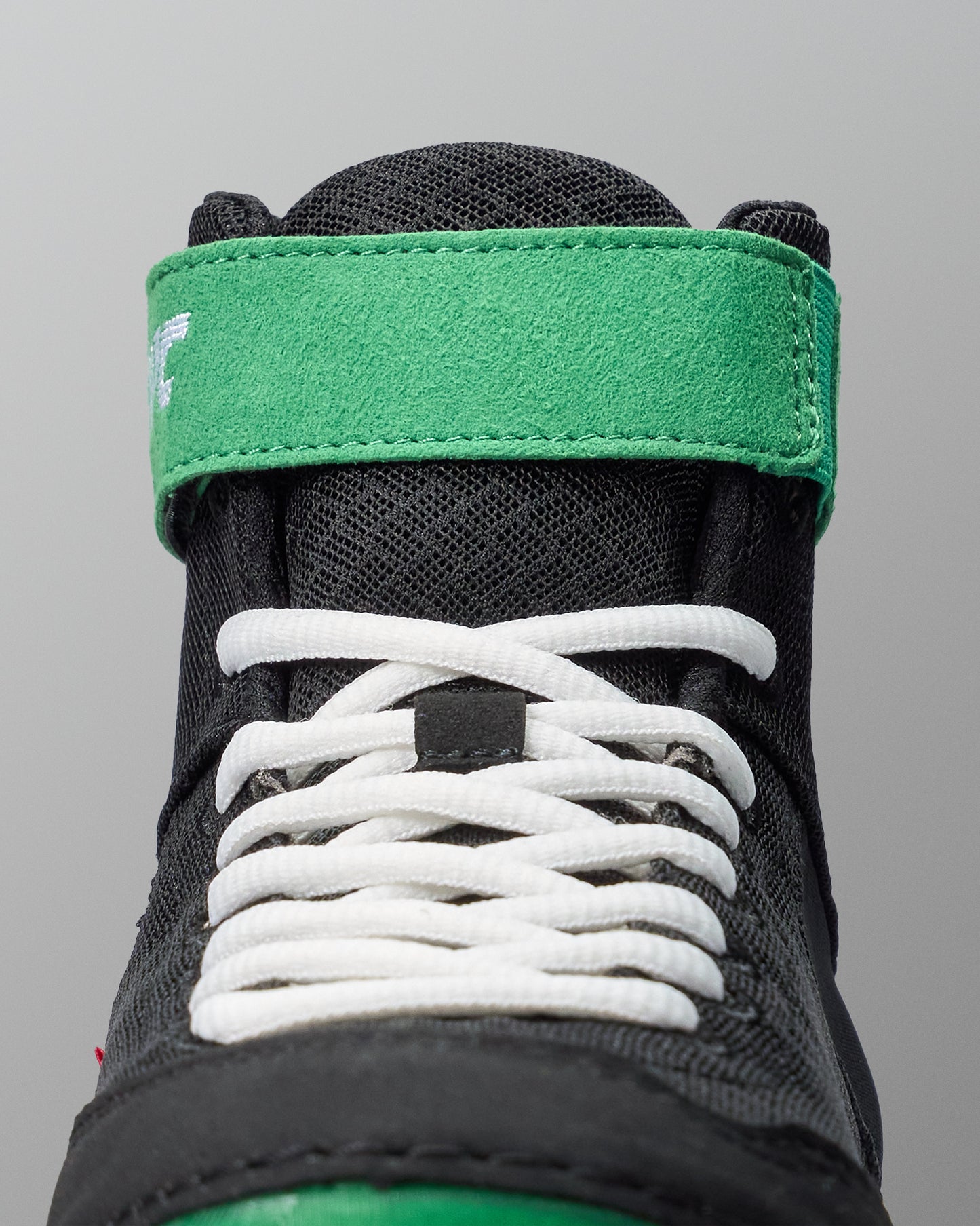 Close-up of a black wrestling shoe with white laces and green accents on a gray background