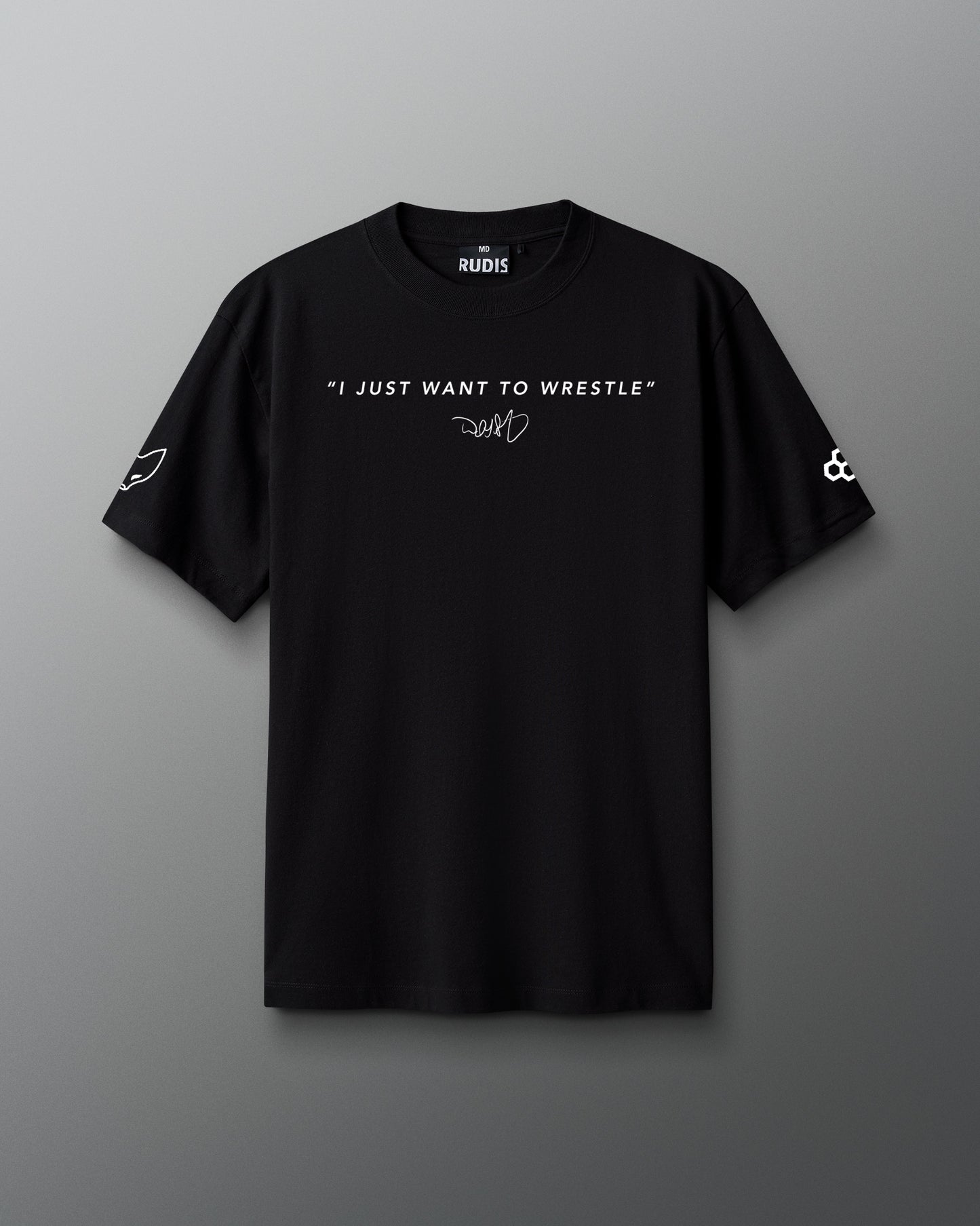 Front view of a black RUDIS t-shirt featuring the quote “I JUST WANT TO WRESTLE” in white capital letters across the chest, with a signature-style graphic underneath. The left sleeve displays a stylized fox head icon, and the right sleeve features the RUDIS hex logo.