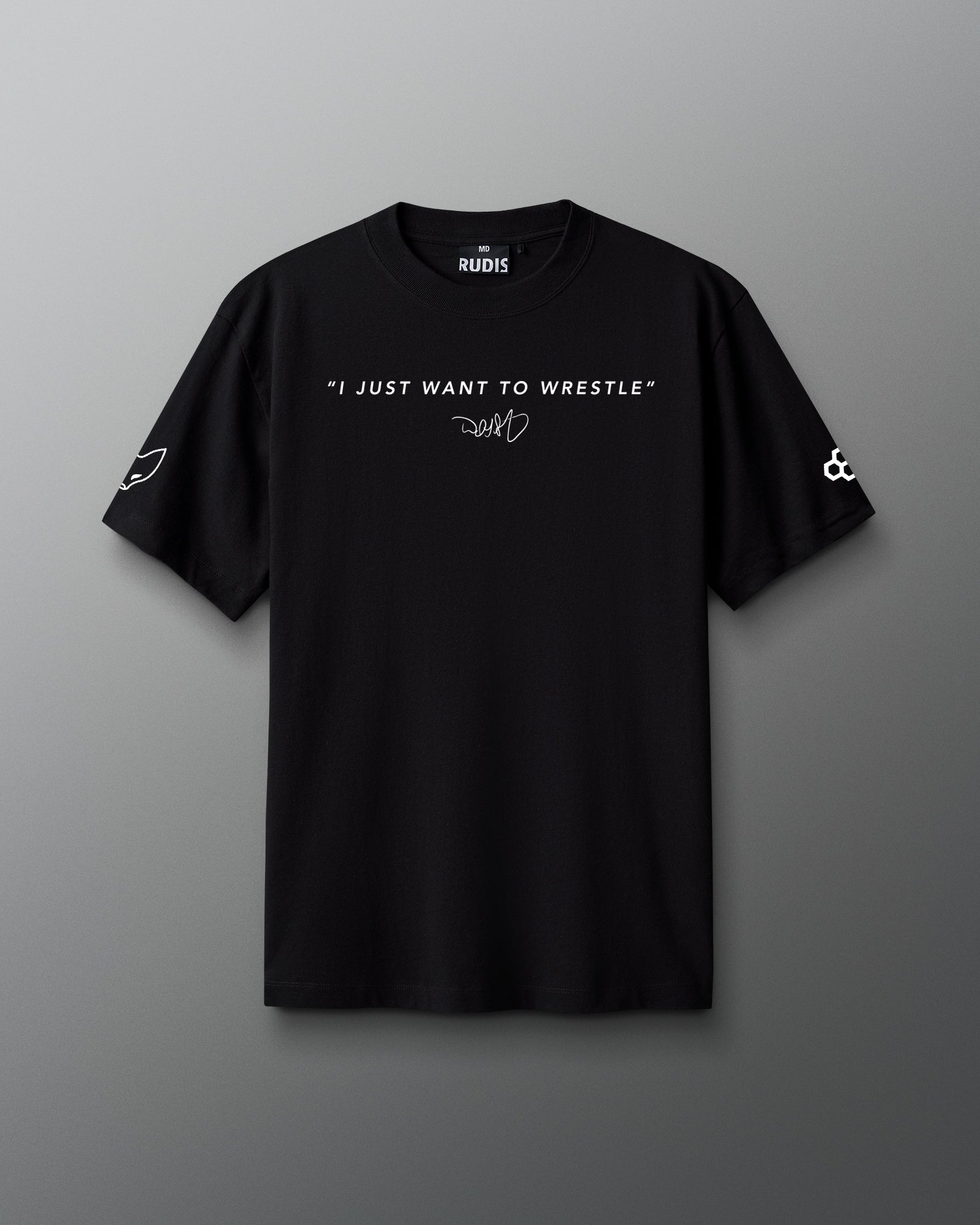 Front view of a black RUDIS t-shirt featuring the quote “I JUST WANT TO WRESTLE” in white capital letters across the chest, with a signature-style graphic underneath. The left sleeve displays a stylized fox head icon, and the right sleeve features the RUDIS hex logo.