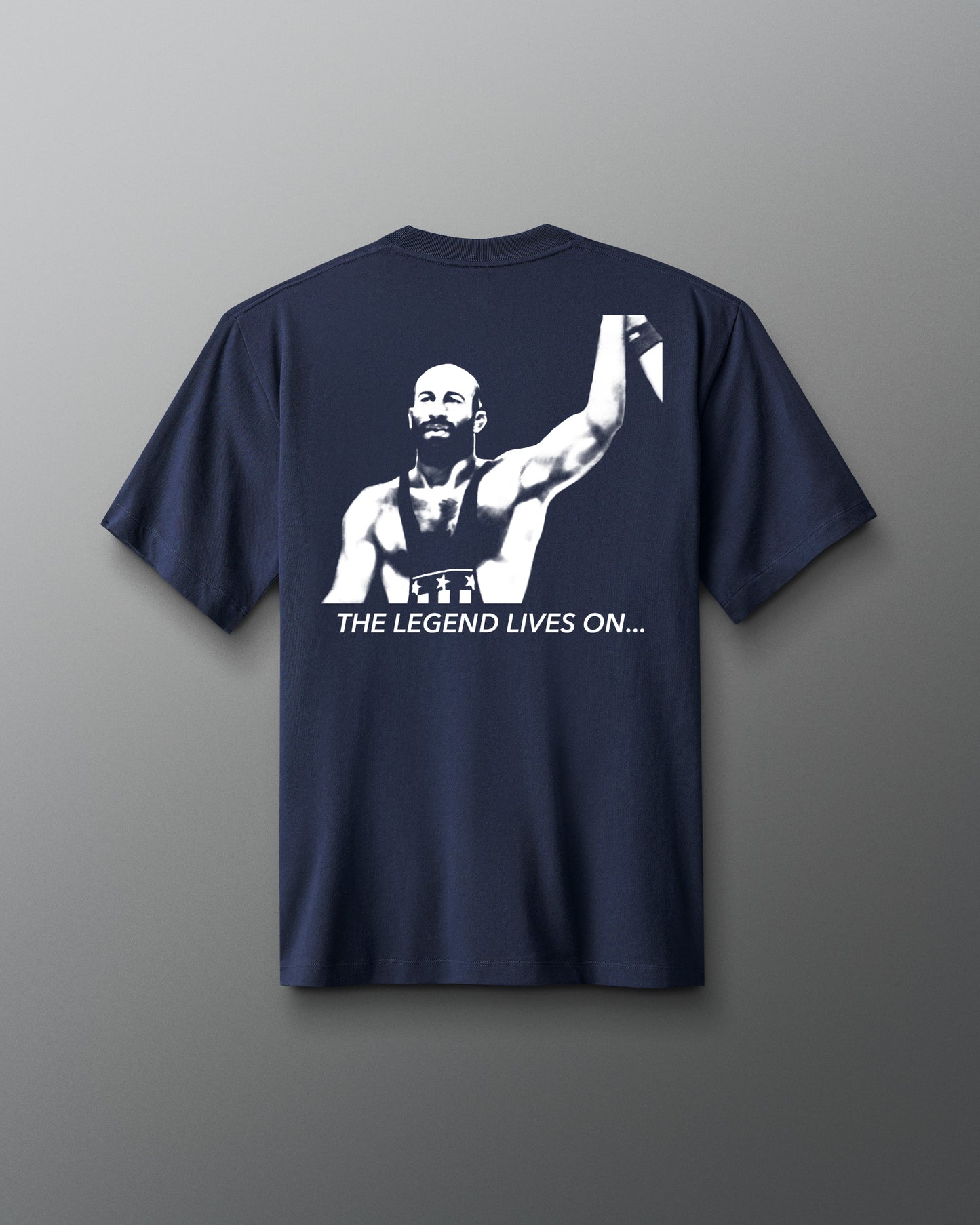 Back view of a navy t-shirt featuring a bold, high-contrast graphic of a victorious wrestler raising his arm. Below the image, the phrase “THE LEGEND LIVES ON…” is printed in white capital letters.