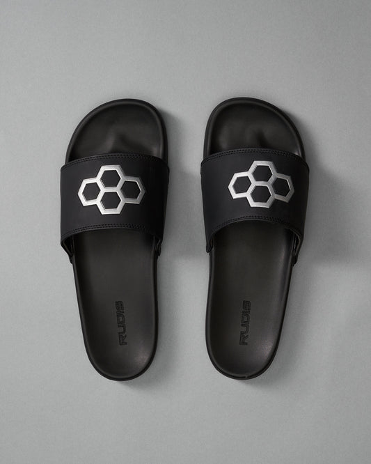 Black slide sandals with a honeycomb design and 'RUDIS' branding, showcased against a soft gray background.