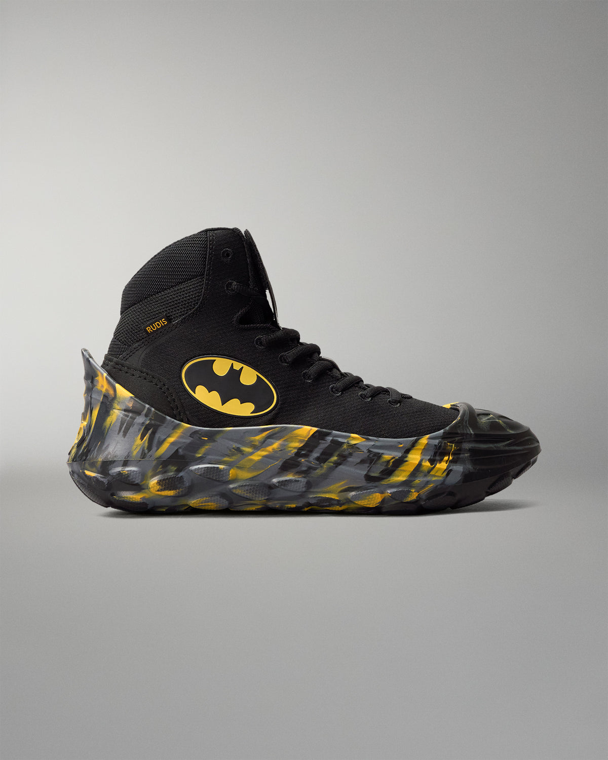 Side view of a black Batman wrestling shoe fitted with RUDIS black and yellow wrestling shoe covers.