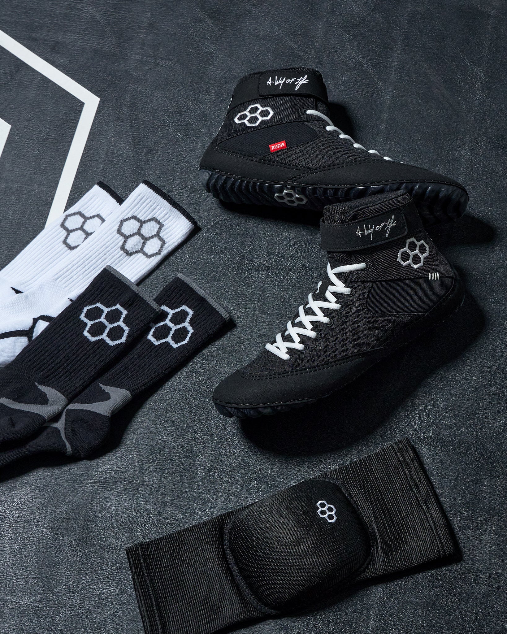 Black wrestling shoes and socks with a RUDIS brand logo on a dark textured surface