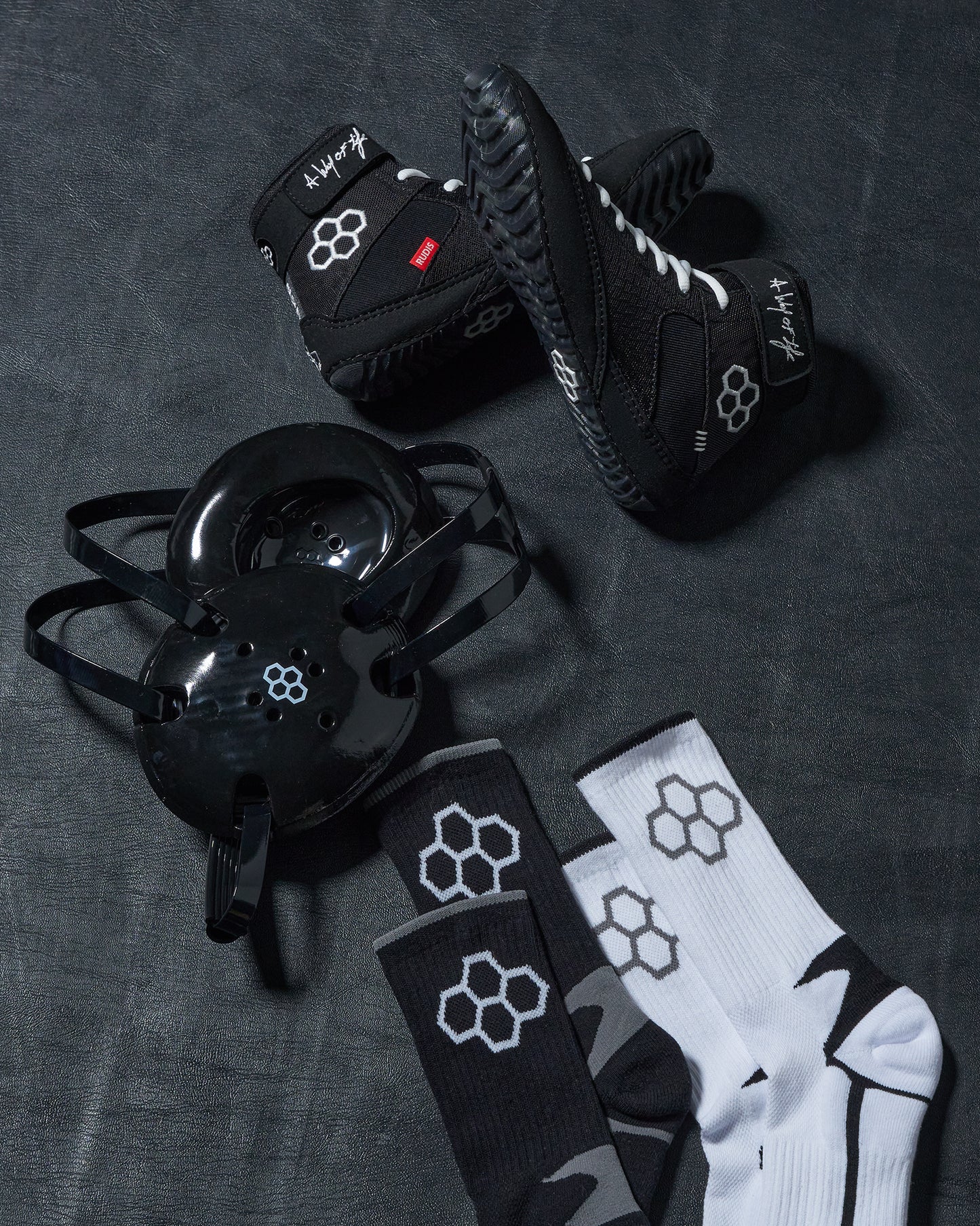 Black wrestling shoes, headgear, and socks with a logo on a dark textured surface