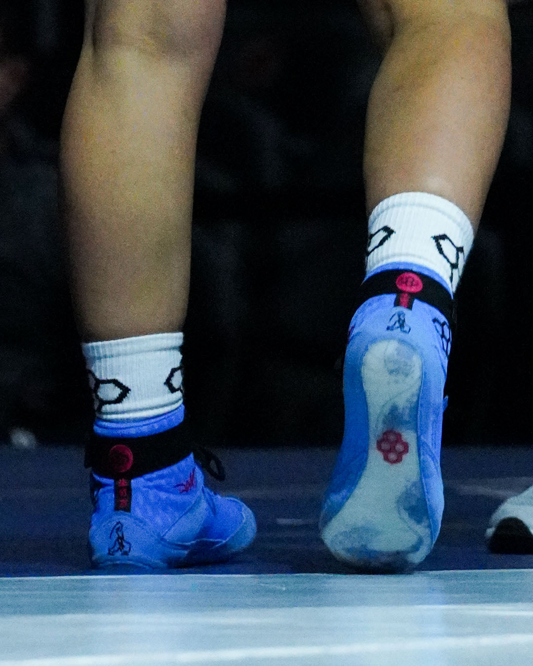 Blue wrestling shoes with white socks featuring black and red designs on a dark background