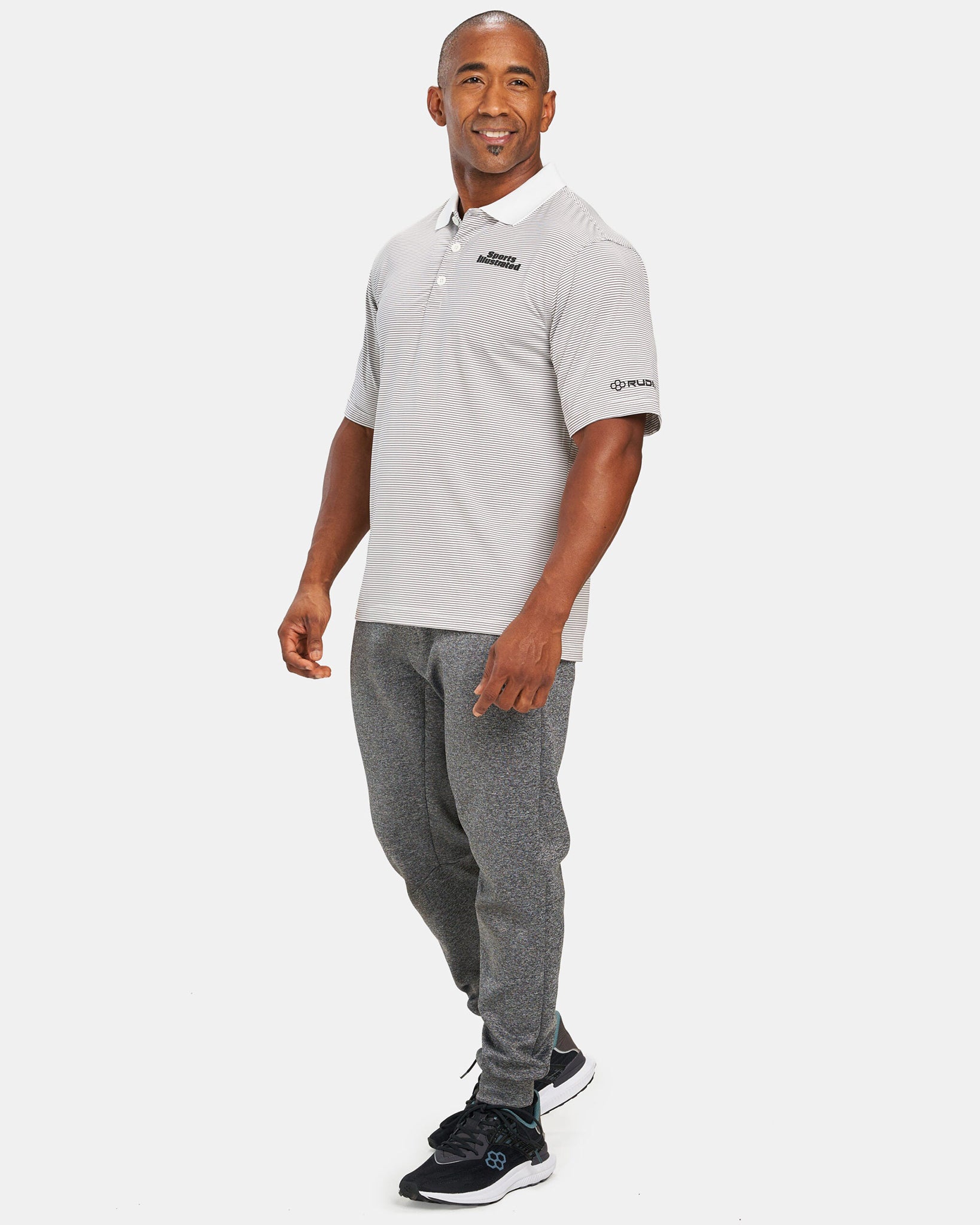 A man wearing a gray striped polo shirt and gray sweatpants poses confidently showcasing a modern athletic outfit paired with black sports shoes