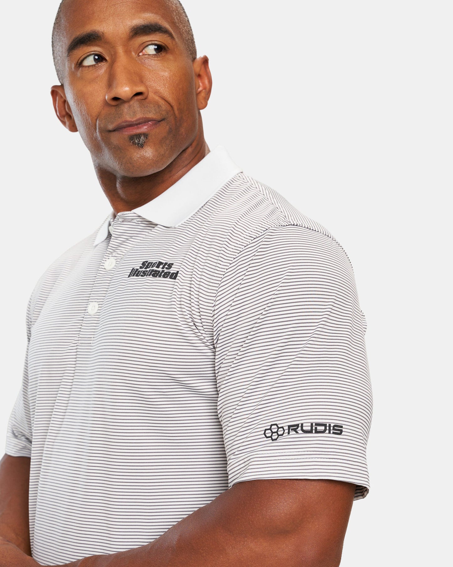 A man in a striped polo shirt featuring the Sports Illustrated logo looks thoughtfully to the side with a slight smile