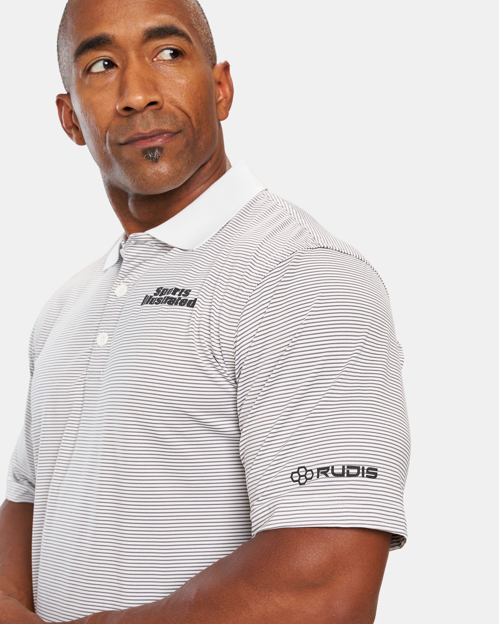 A man in a striped polo shirt featuring the Sports Illustrated logo looks thoughtfully to the side with a slight smile