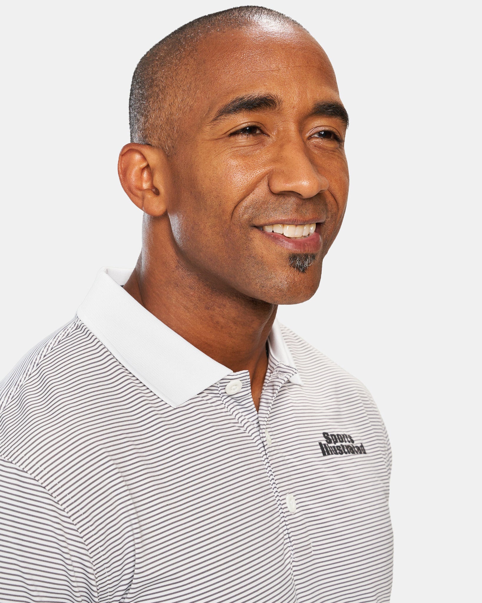 A smiling man with a close-cropped hairstyle wearing a striped polo shirt featuring a logo on the chest