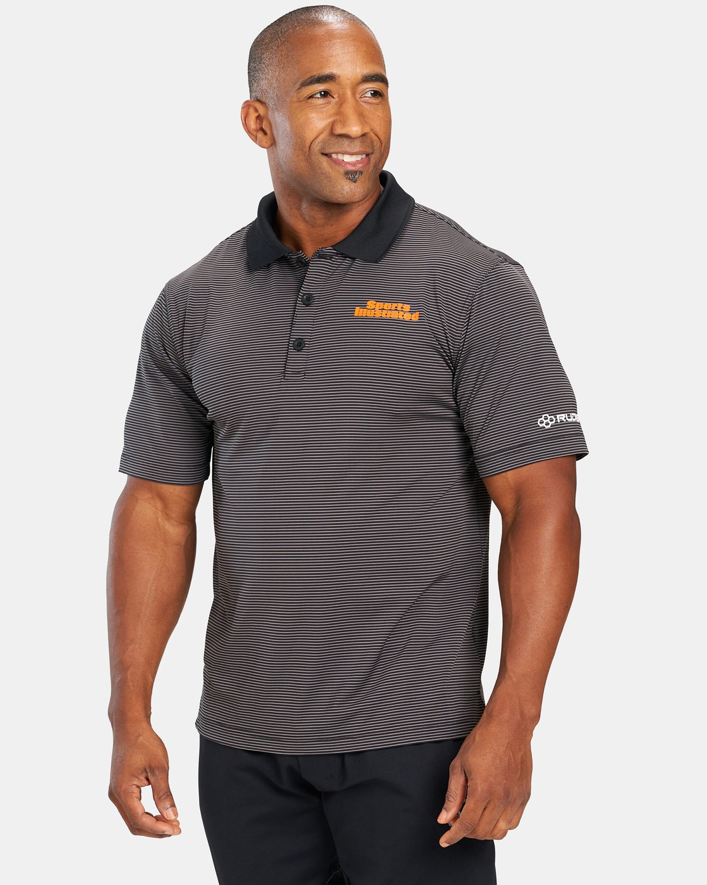 A smiling man is wearing a black and gray striped polo shirt with the text Sports Illustrated and a logo on the sleeves standing against a plain background