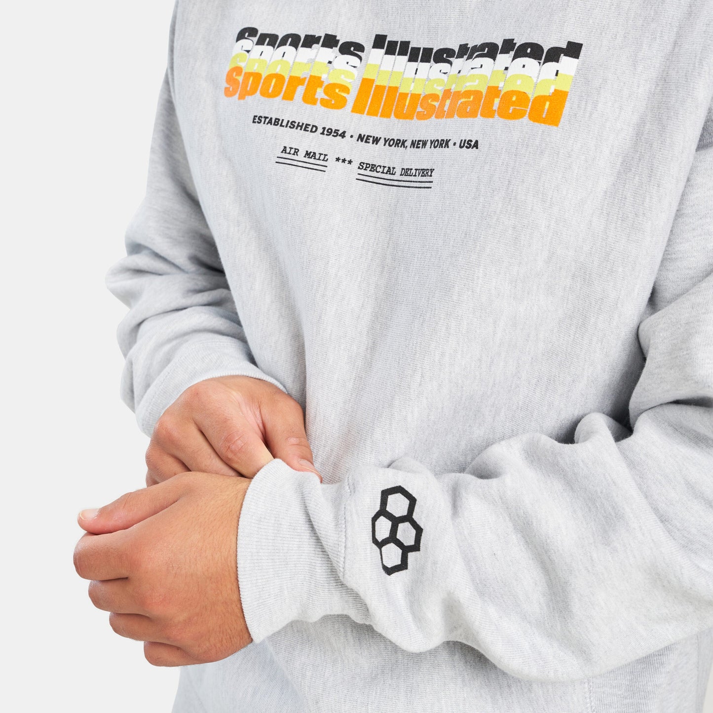 A close-up of a person wearing a light gray sweatshirt featuring the bold Sports Illustrated logo and a distinct graphic on the sleeve