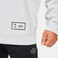 A close-up shot of a mans hand holding the cuff of a light gray sweatshirt featuring a logo patch that includes SI and the year 1954