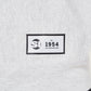 A label on a light gray sweatshirt featuring a black rectangular patch with the text SI EST 1954 NEW YORK NEW YORK