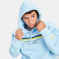 A young man wearing a light blue hoodie with bold graphic text and a playful design adjusting the hood of his sweatshirt