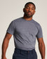 A confident man poses in a fitted gray t-shirt and navy blue pants showcasing a casual yet stylish look against a neutral background