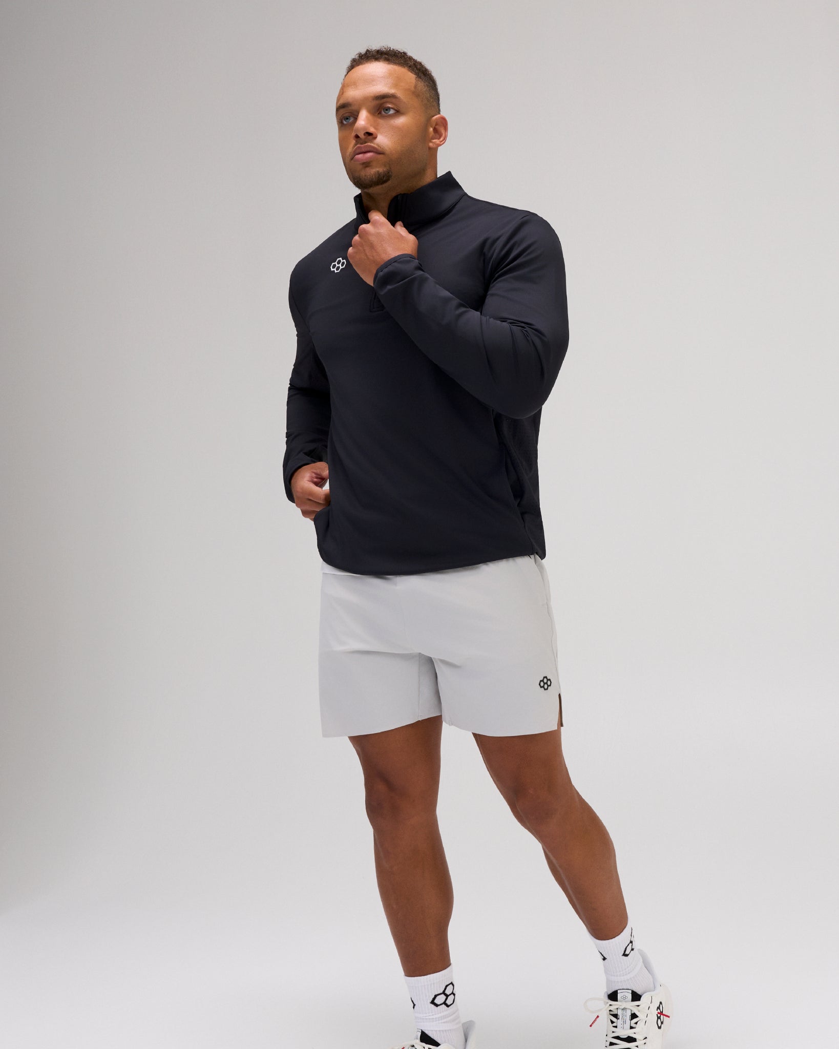 Model wearing the black RUDIS Victory 1/4 Zip performance pullover with light gray athletic shorts and white training shoes.