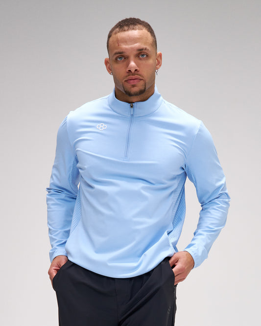 Man wearing a light blue long-sleeve athletic shirt with a brand logo on a gray background