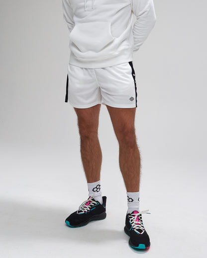 Person wearing white shorts with black accents and black athletic shoes on a plain background