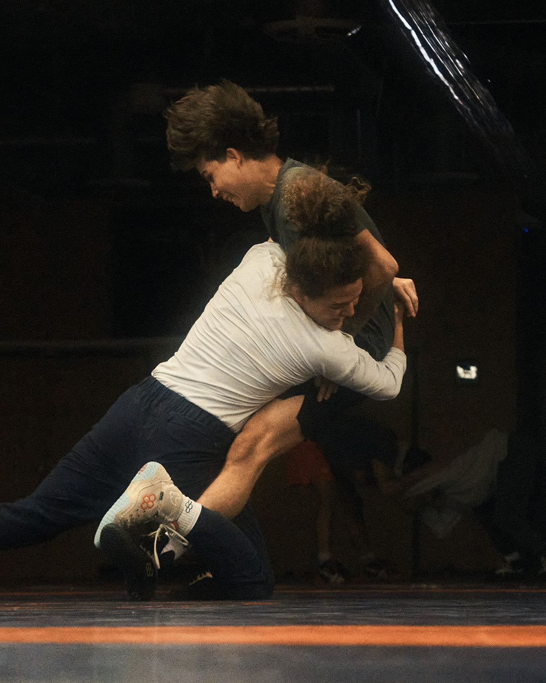 Intense wrestling training session featuring athletes in RUDIS gear, with one wrestler driving into a powerful takedown while wearing RUDIS wrestling shoes – capturing strength, speed, and technique on the mat.