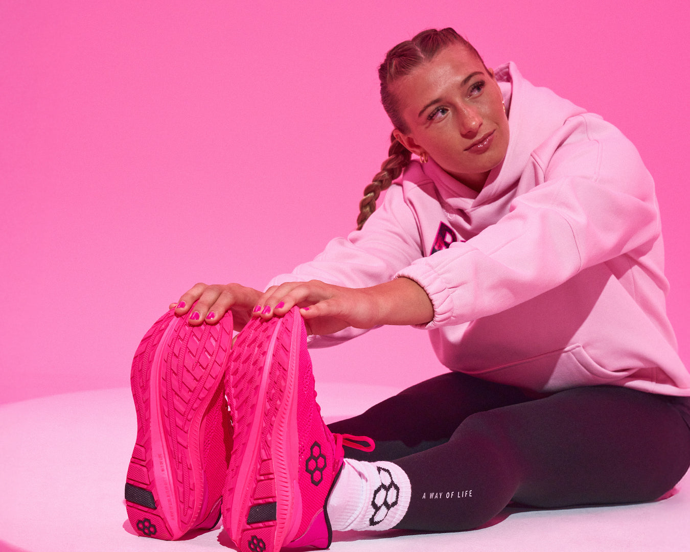 Team USA wrestler Kylie Welker stretching in bold pink RUDIS training shoes, black leggings, and a pink RUDIS hoodie, set against a bright pink backdrop – showcasing athletic style, comfort, and women’s wrestling lifestyle.