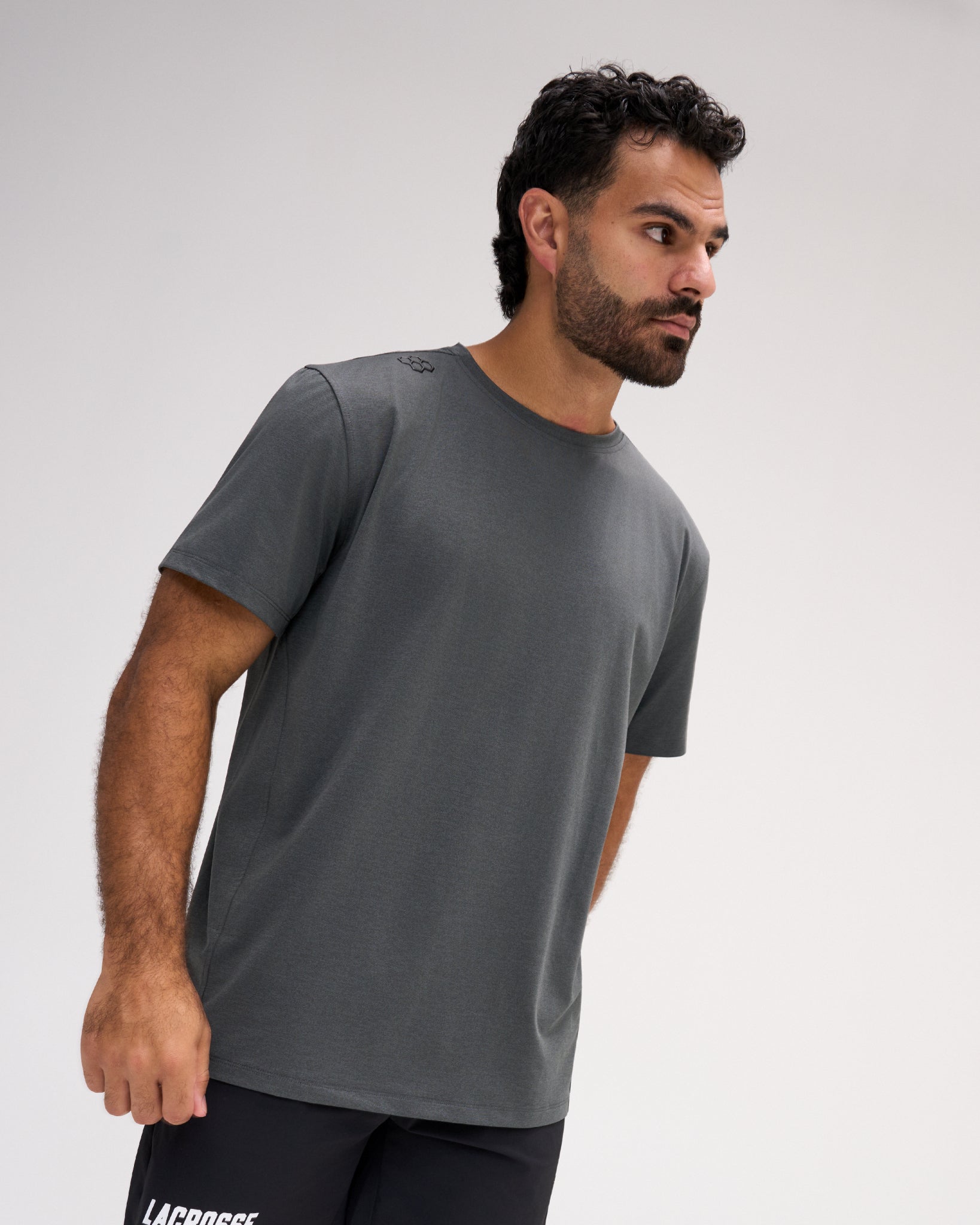 Model wearing the RUDIS Performance Heather T-Shirt in Heather Carbon, featuring medium-gray heathered fabric, short sleeves, a crew neckline, and subtle RUDIS shoulder branding.