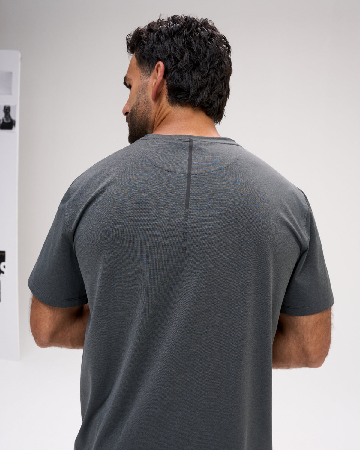 Back view of the RUDIS Performance Heather T-Shirt in Heather Carbon, showcasing gray heathered fabric, a vertical upper-back graphic, and classic short-sleeve construction.