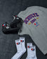 Gray t-shirt with 'Schultz 1984' design, black wrestling shoes, and white socks on a dark surface