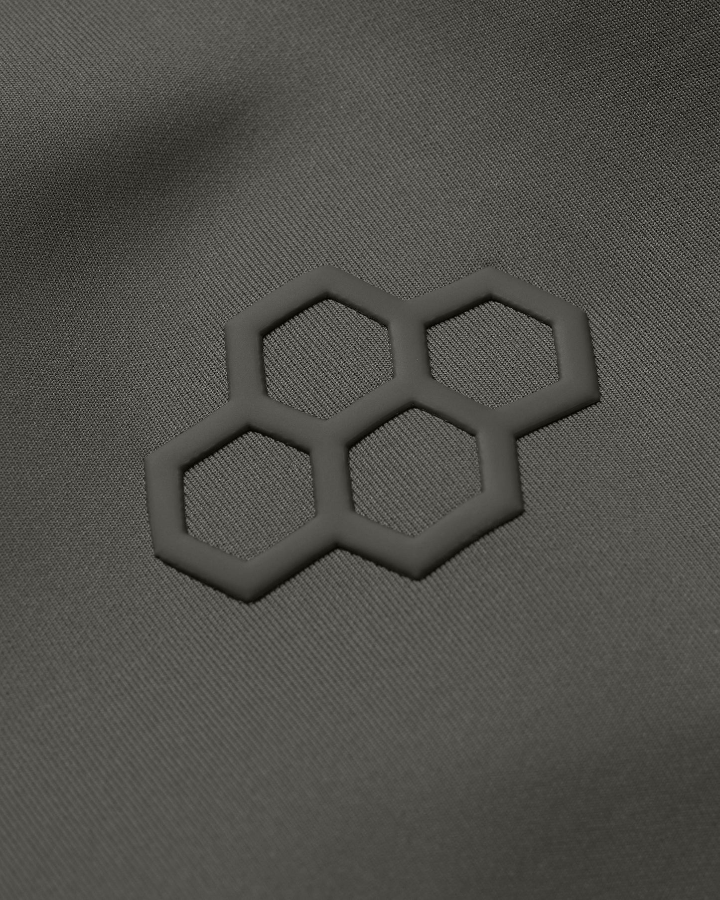 Dark olive green fabric showcases a textured surface with a subtly raised hexagonal pattern, hinting at modern and functional design suited for outdoor or athletic wear.