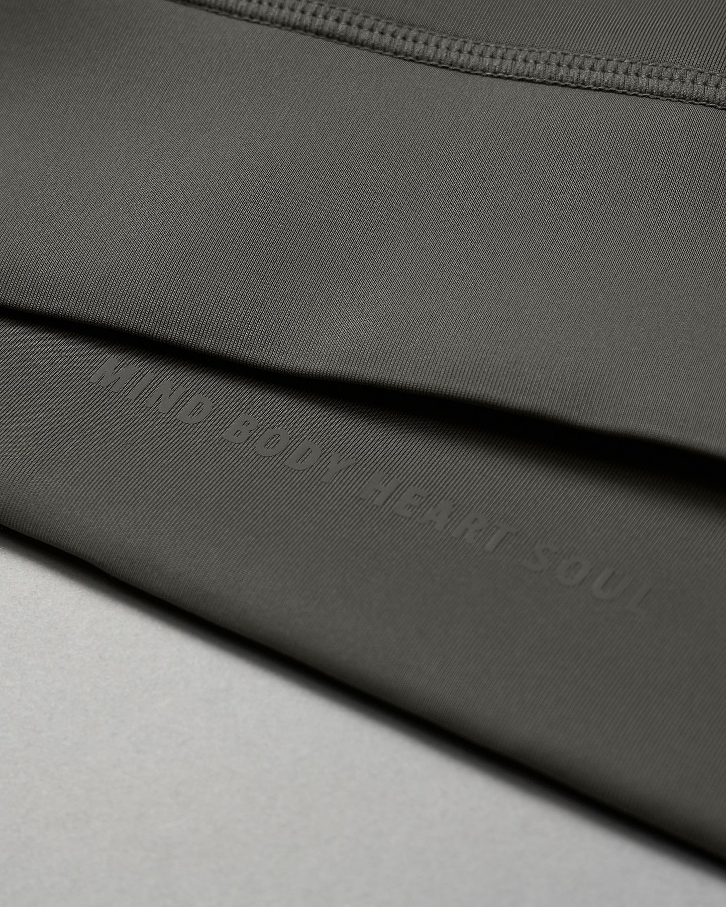 An olive green fabric with a smooth texture features a subtle inscription of 'MIND BODY HEART SOUL', highlighting a wellness theme.