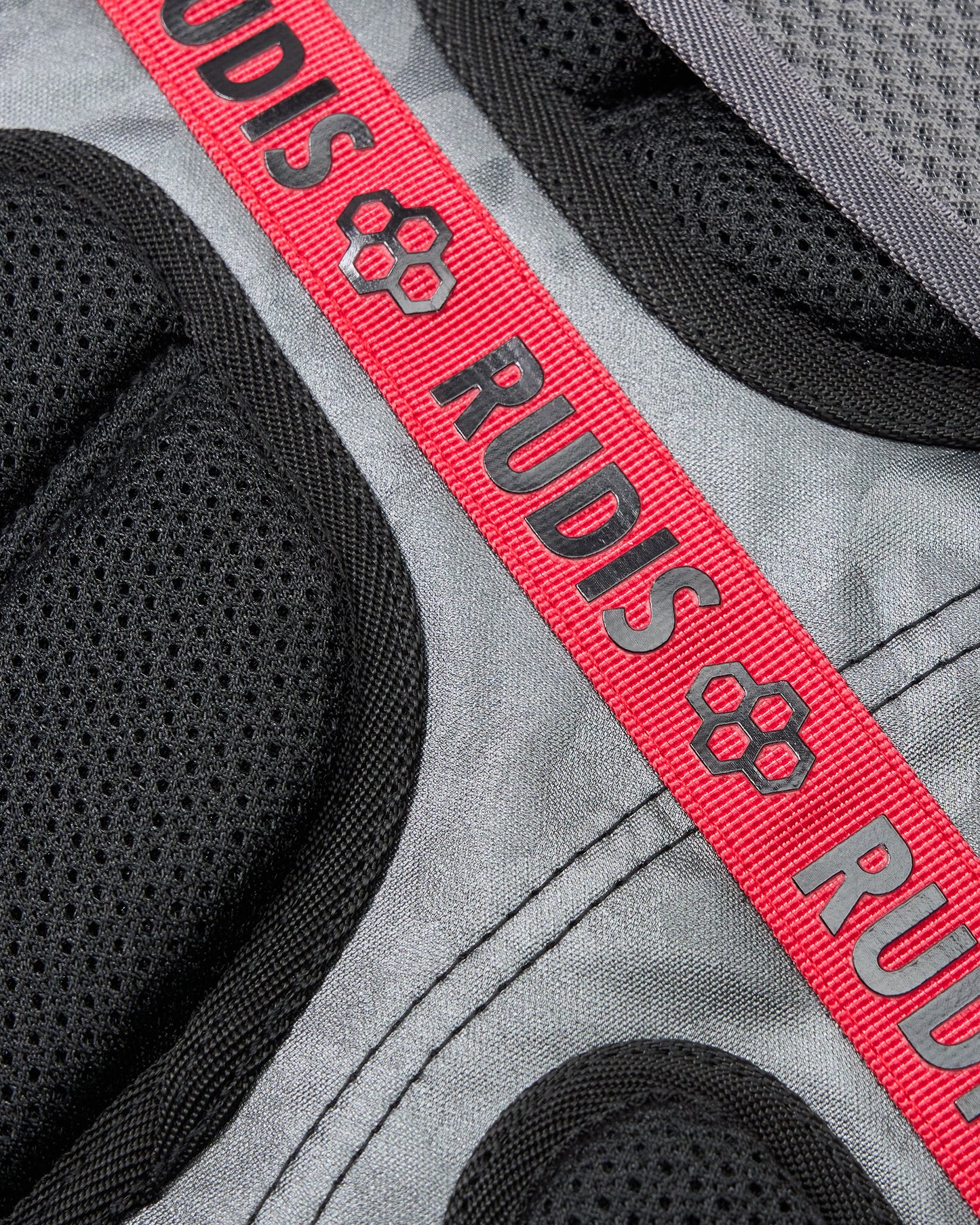 Close-up of a gray and black backpack with a red 'RUDIS' strap.