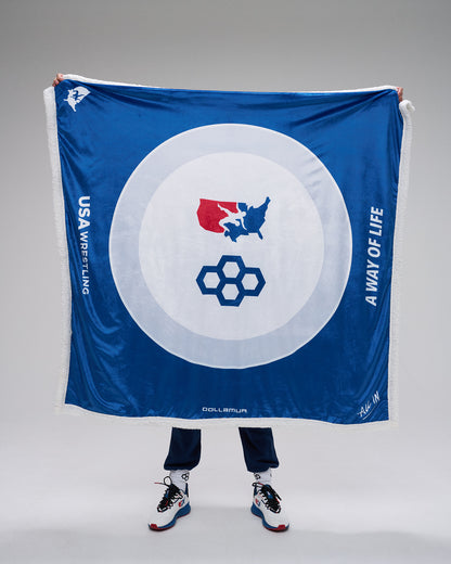 Person holding a blue blanket with a circular emblem featuring a flag and geometric design, on a gray background.