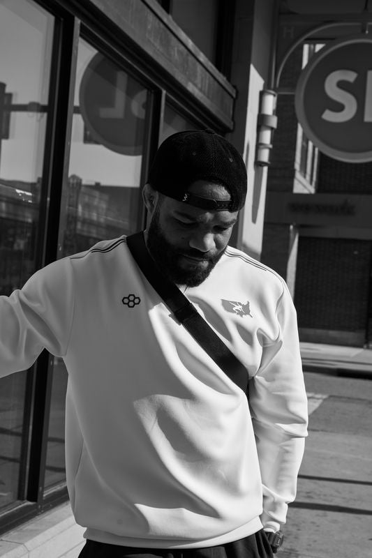 Man wearing a white sweatshirt with USA Wrestling and RUDIS logos in an urban setting