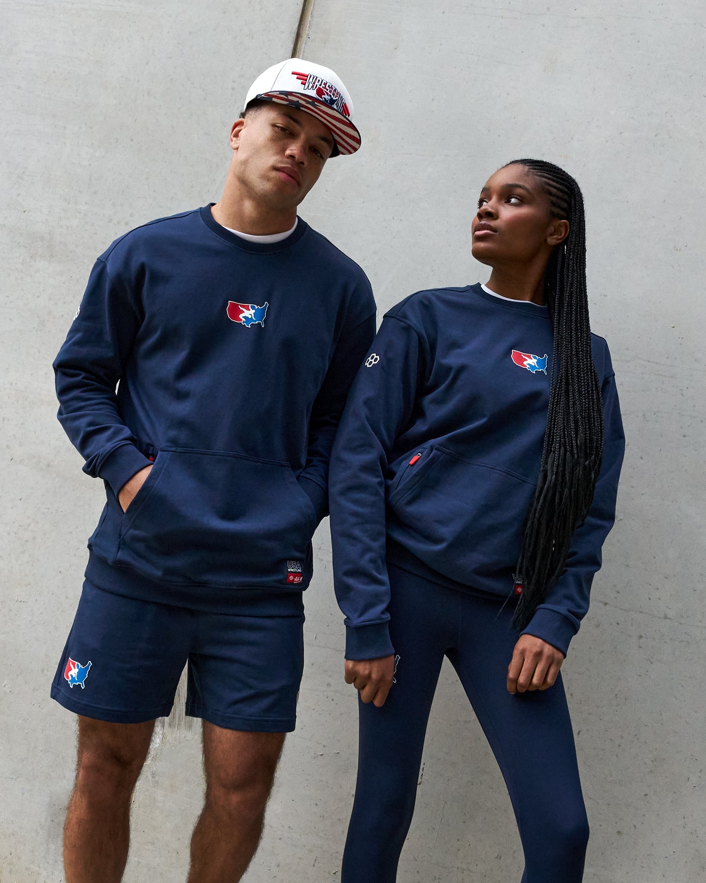Two people wearing matching navy blue outfits with logos against a gray wall.