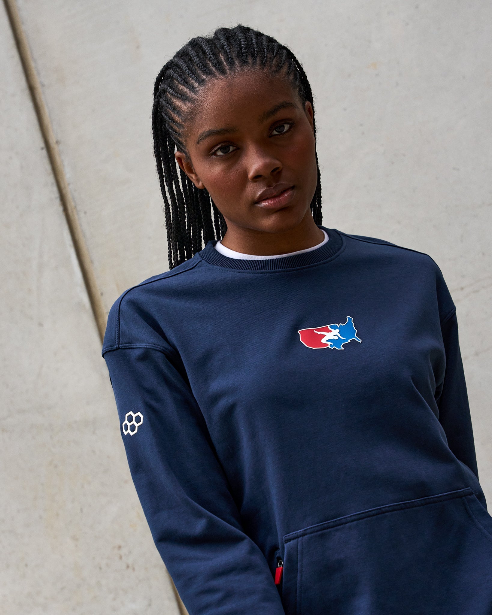 Person wearing a navy blue sweatshirt with a logo against a light gray background