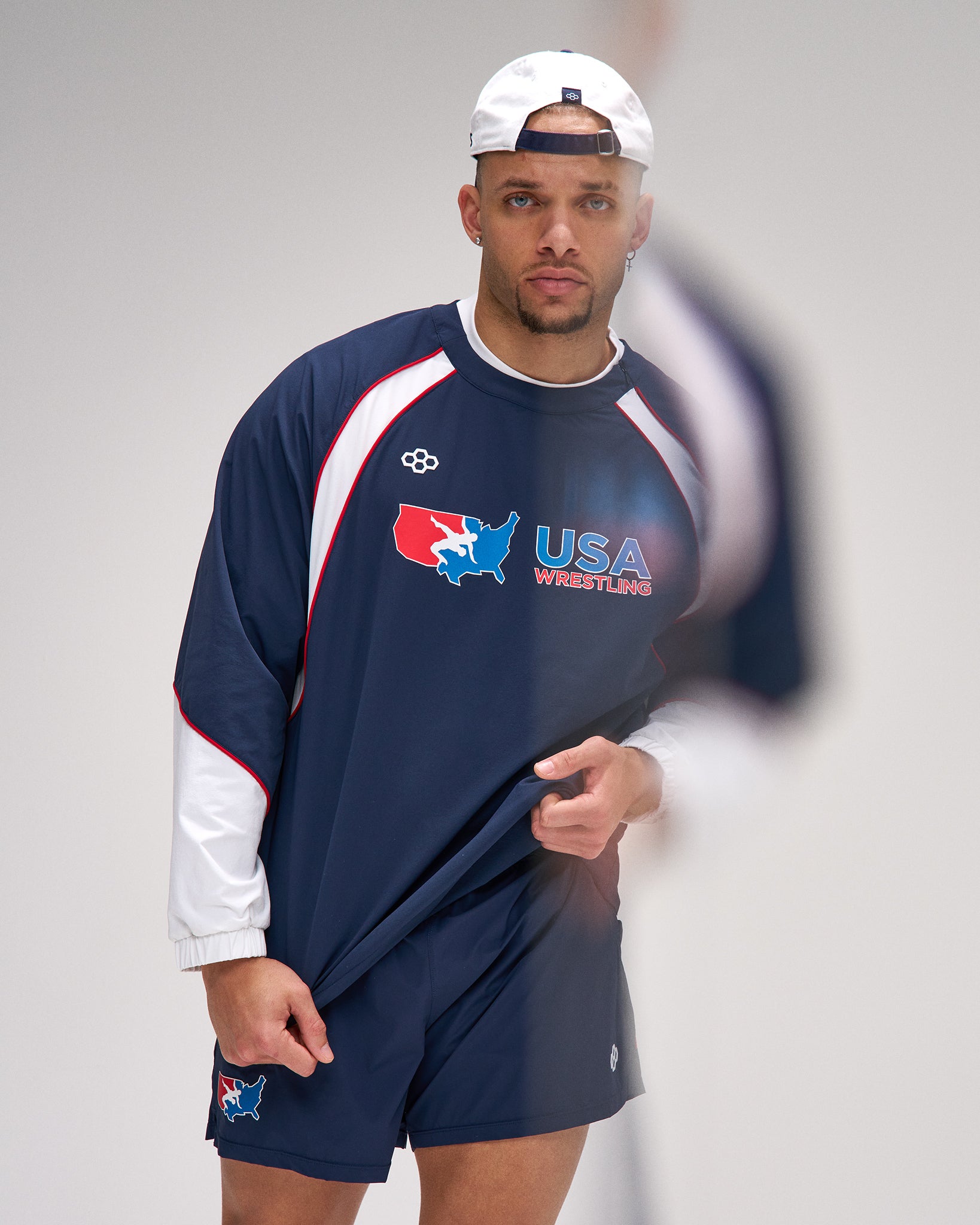 Man wearing a USA Wrestling tracksuit and cap on a plain background
