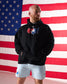Man wearing a black hoodie with a logo in front of an American flag