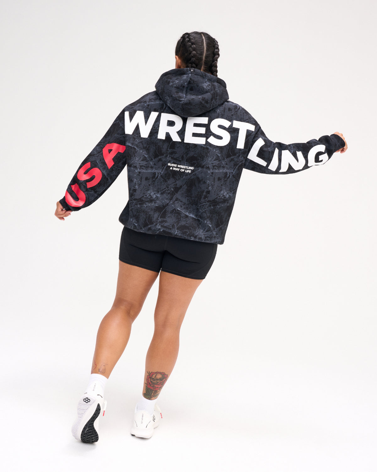 Back view of female model wearing the RUDIS USA Wrestling Map fleece hoodie in Black Camo, featuring oversized white WRESTLING lettering and red USA sleeve graphics.