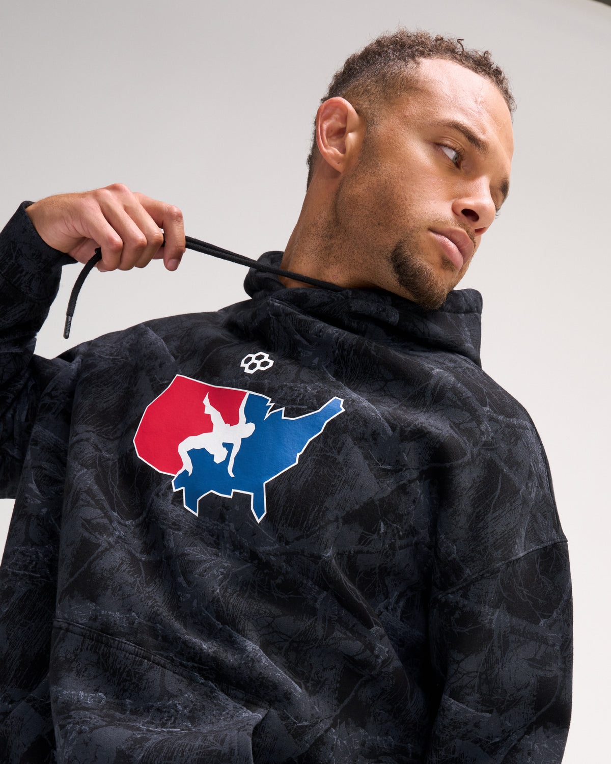 Close-up of male model wearing the RUDIS USA Wrestling Map hoodie in Black Camo, highlighting the red, white and blue wrestling map chest graphic and drawstring hood.