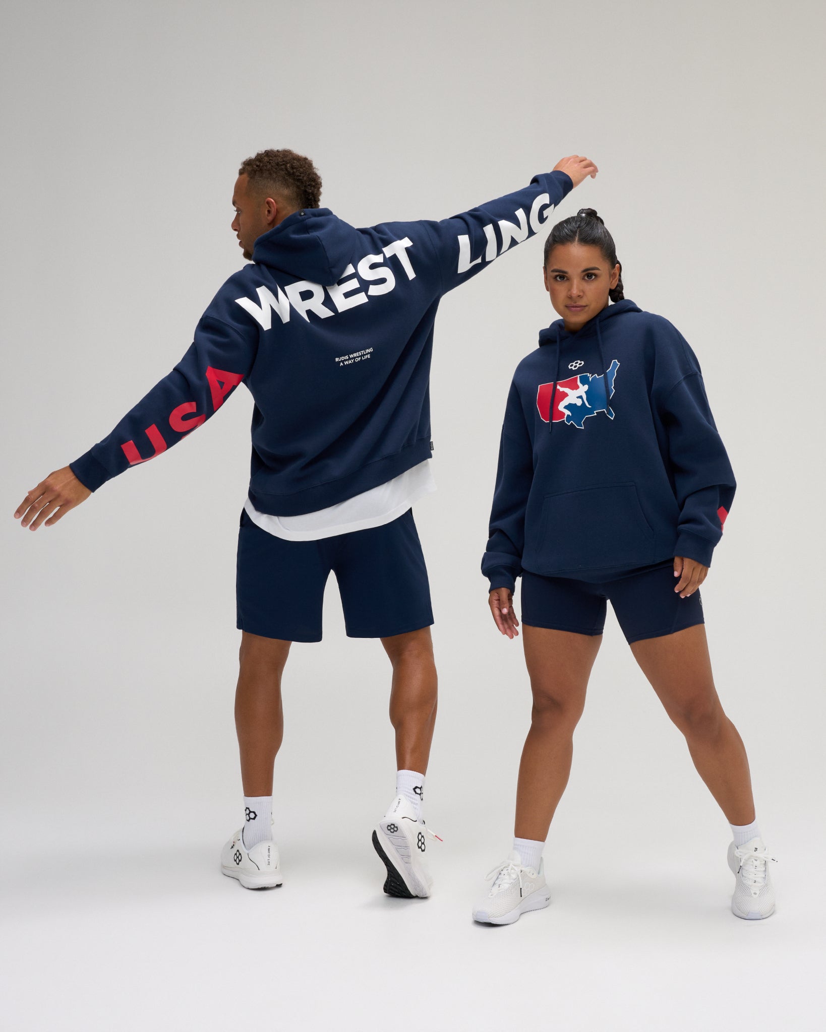 Male and female models wearing the RUDIS USA Wrestling Map Relaxed Comfort Fleece Hoodie in Navy, showcasing the patriotic chest logo and bold USA WRESTLING sleeve and back graphics.