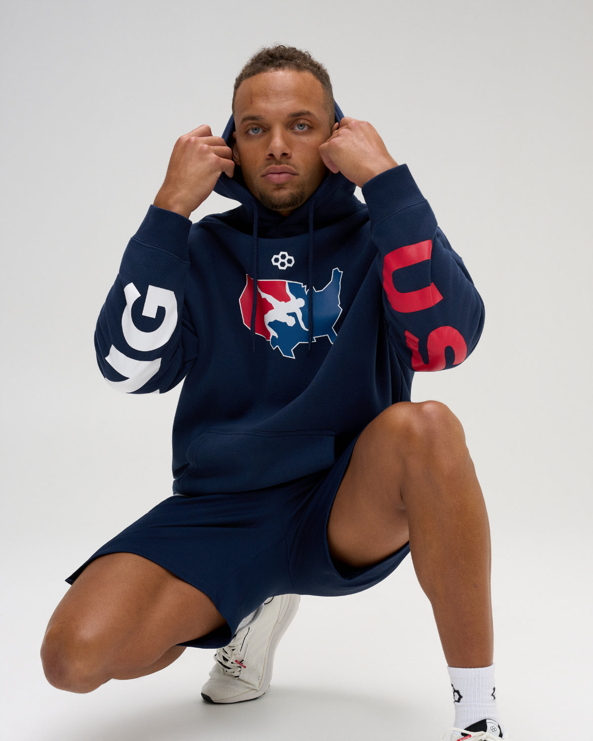 Male model wearing the RUDIS USA Wrestling Map Relaxed Comfort Fleece Hoodie in Navy, showing the red, white and blue map graphic, USA sleeve lettering and kangaroo pocket.